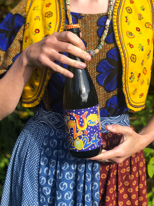 Person in colorful traditional attire holding a bottle of cider with a decorative label.