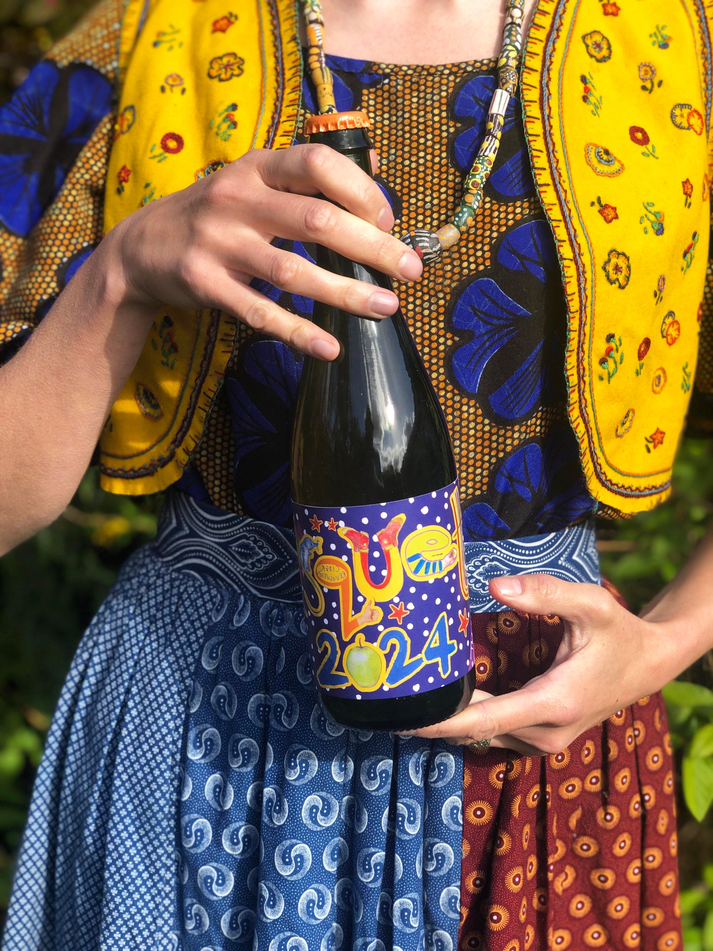 Person in colorful traditional attire holding a bottle of cider with a decorative label.