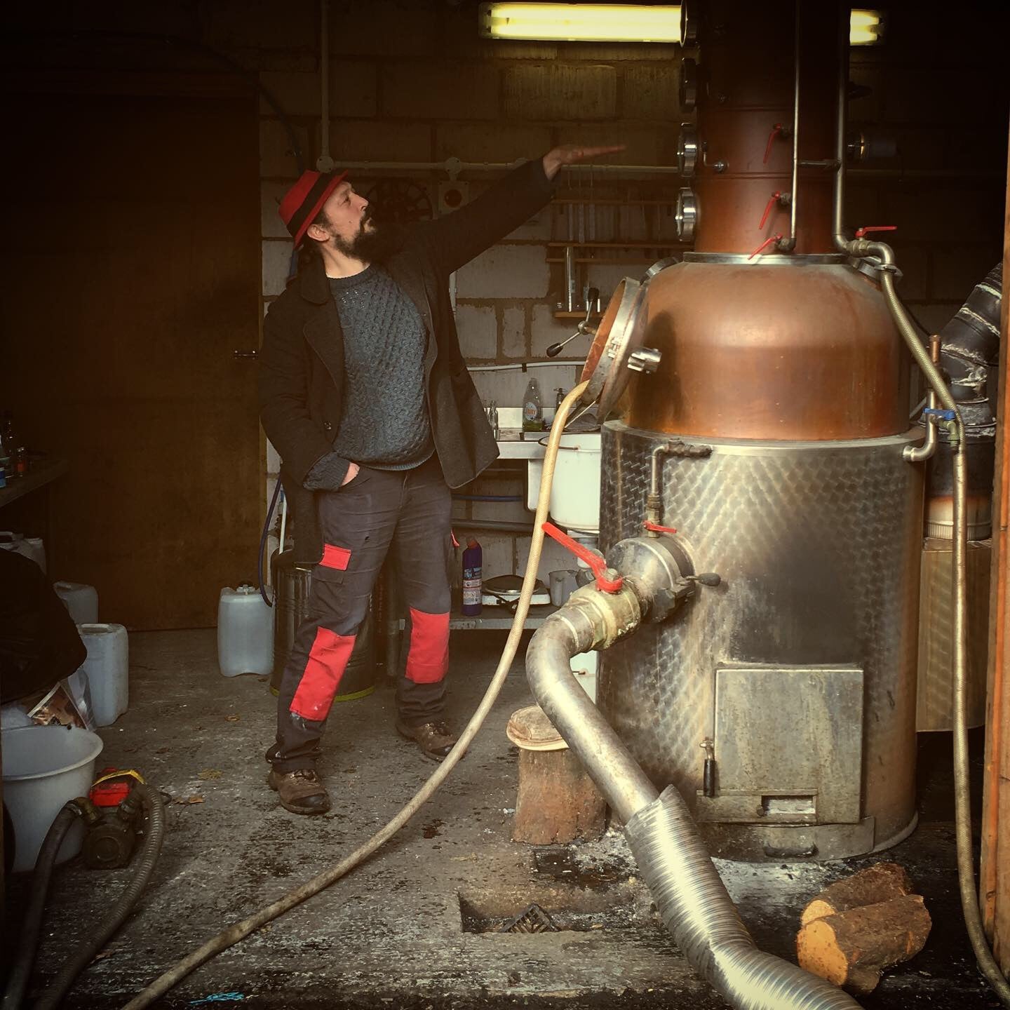 Person standing next to a large copper still in a workshop setting