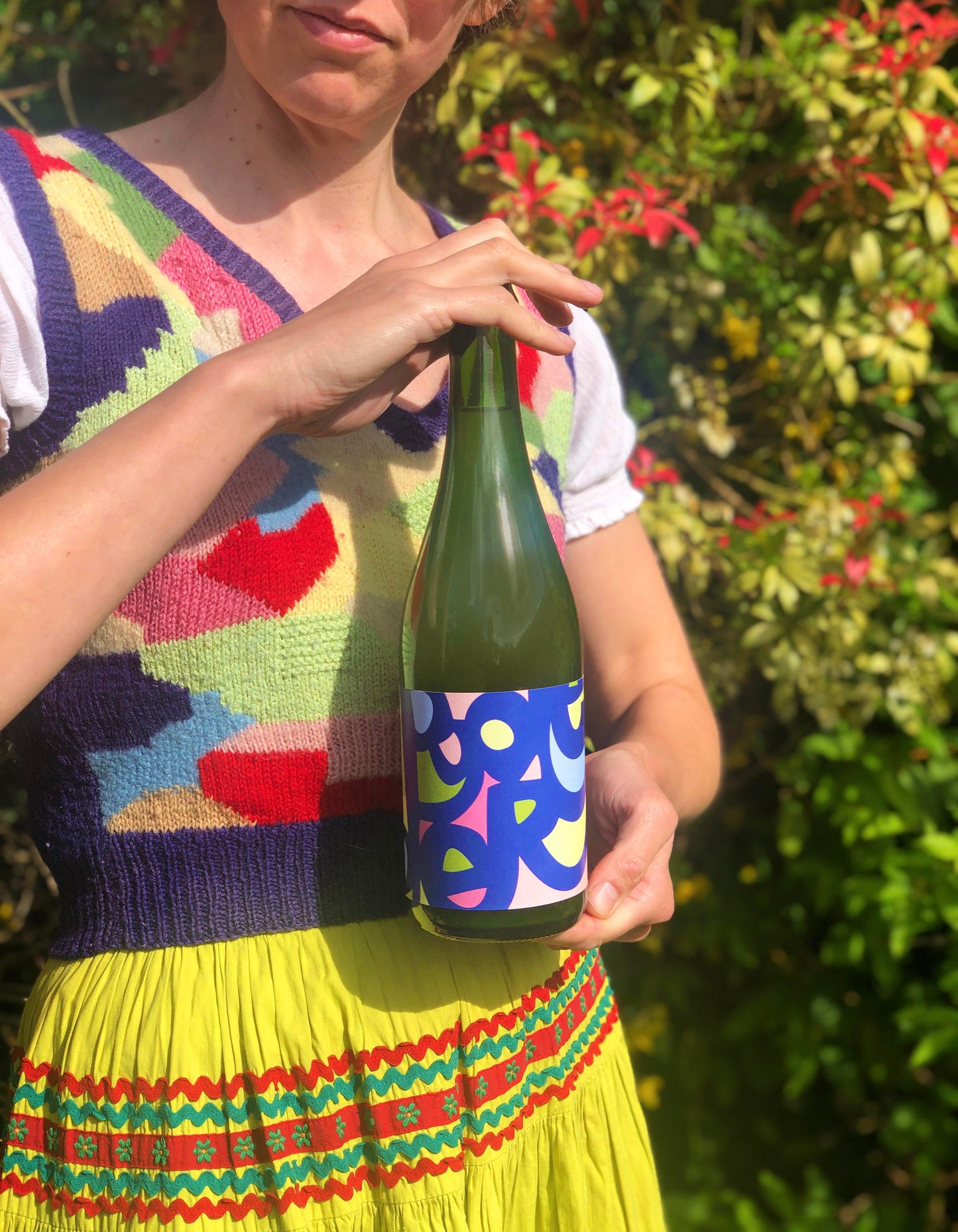 Person holding a green bottle with colorful label outdoors
